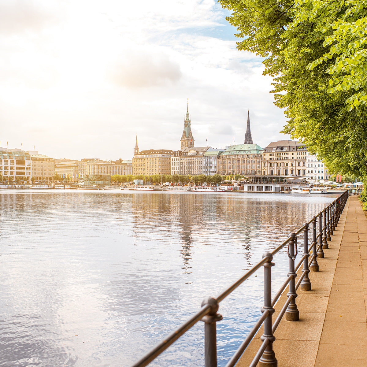 Blick über die Hamburger Innenalster mit Uferpromenade, Geländer und Stadtsilhouette im warmen Abendlicht